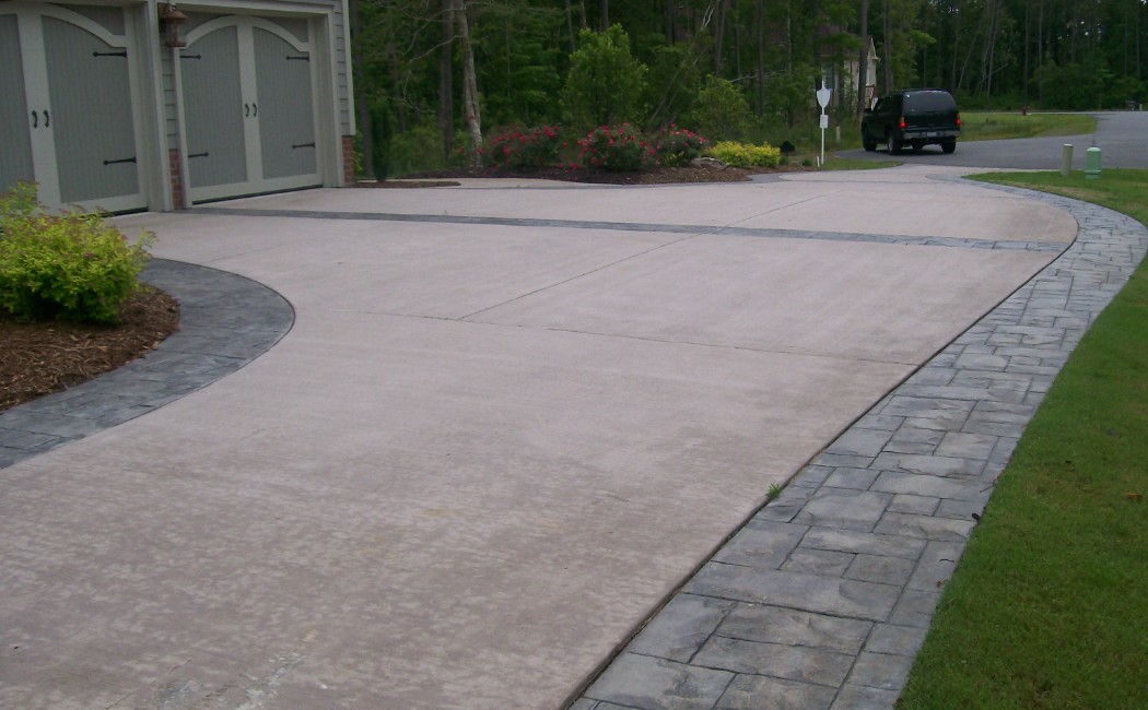 A clean, spacious driveway with decorative stamped concrete borders, highlighting expert Concrete Driveways and Patios Services in a modern suburban setting.