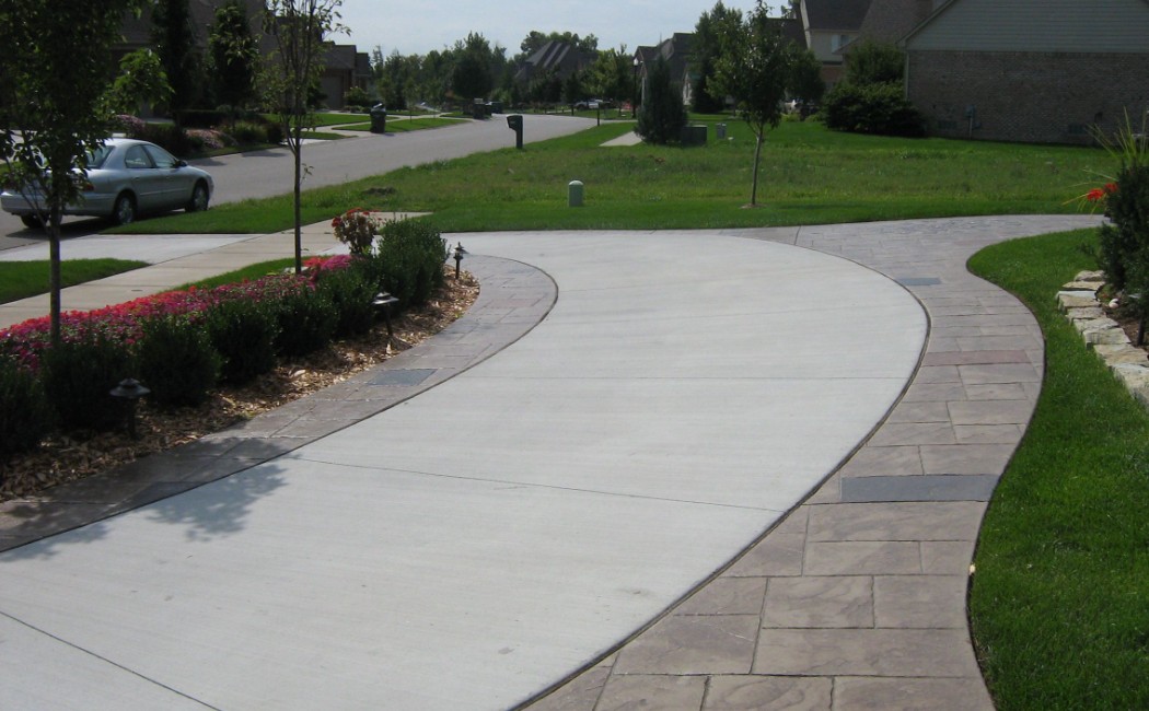 A stylish residential driveway featuring smooth concrete with stamped border detailing, showcasing high-quality Concrete Driveways Services in a suburban neighborhood.