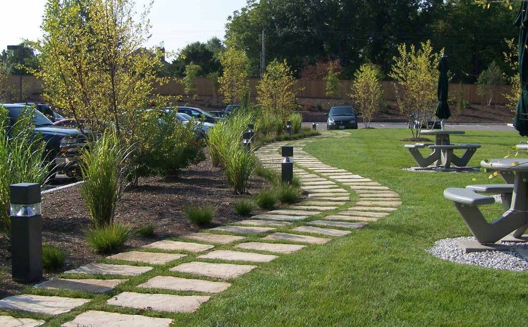 A beautifully designed outdoor area with a stone walkway, green lawn, and seating spaces created by a professional landscaping work company.