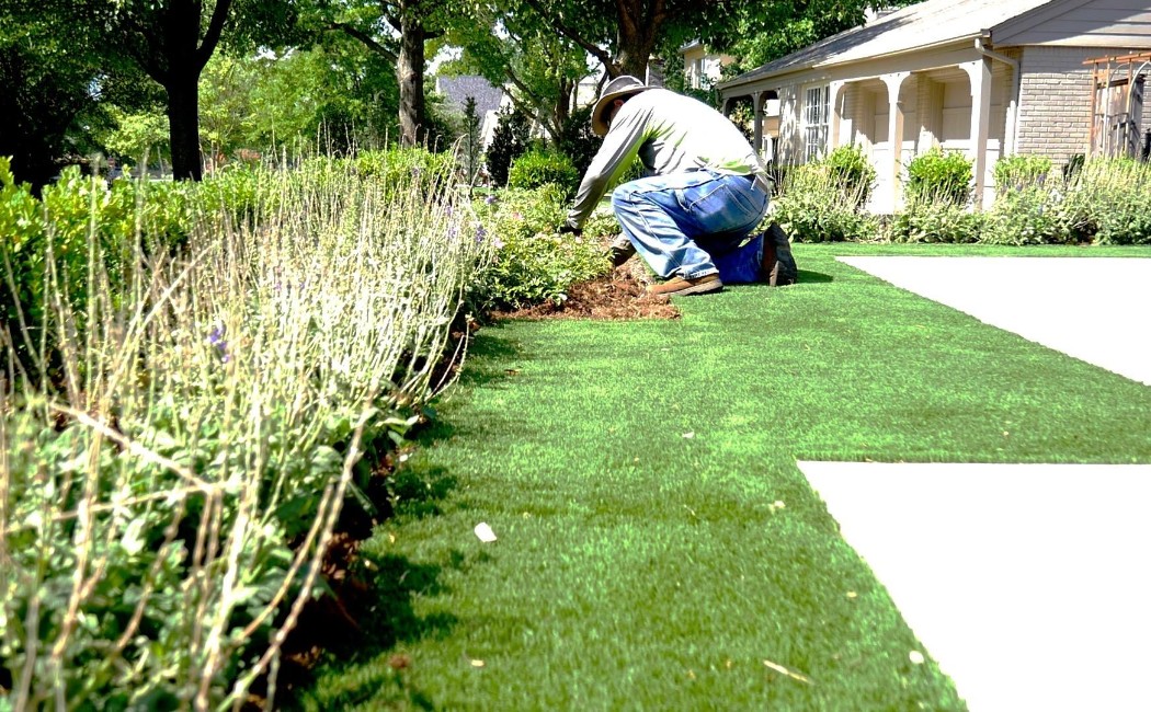 A landscaper works on a garden bed, enhancing the outdoor space with carefully arranged plants and artificial turf. Landscaping Work Company offering professional services for residential gardens