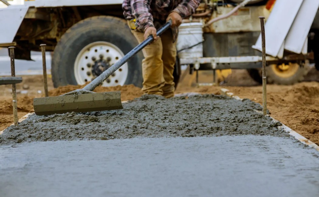 A worker levels freshly poured concrete on a sidewalk or driveway, highlighting the hands-on precision involved in Professional Concrete Services.