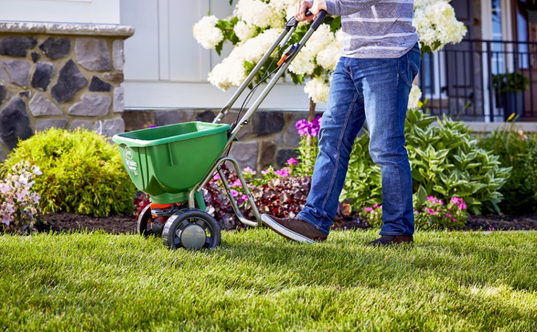 A professional applying lawn treatment using a spreader on healthy green grass, showcasing expert maintenance services by a trusted Lawn Care Company.