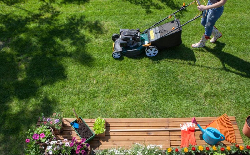 A person mowing a lush green lawn surrounded by flowers and gardening tools, showcasing professional Yard Care Services for a neat and vibrant outdoor space.