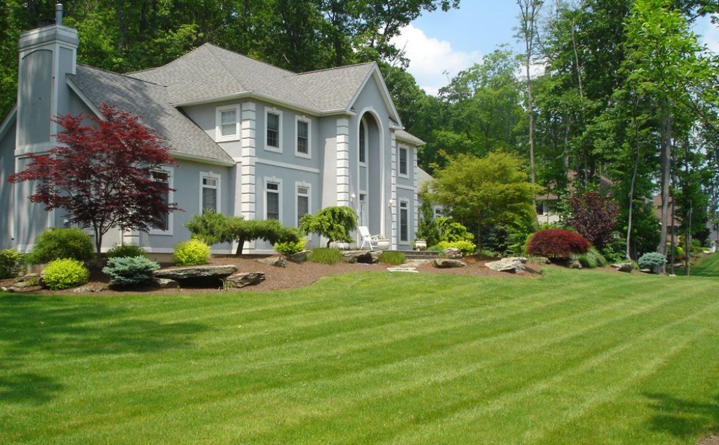 A well-manicured green lawn surrounding a modern home, highlighting the expert maintenance and landscaping services of a professional Lawn Care Company.