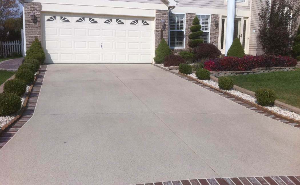 This image showcases a neatly designed concrete driveway with well-maintained landscaping, emphasizing the excellence of concrete driveway services.