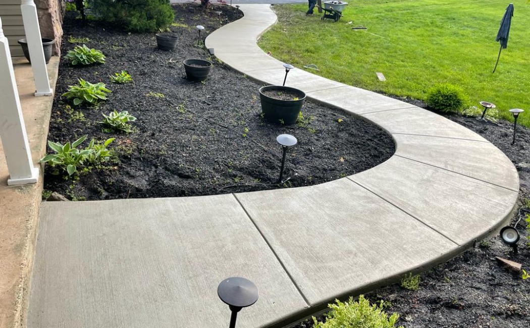 A freshly installed curved concrete walkway enhances the front yard, showcasing the quality and precision of Concrete Sidewalk Services for residential properties.
