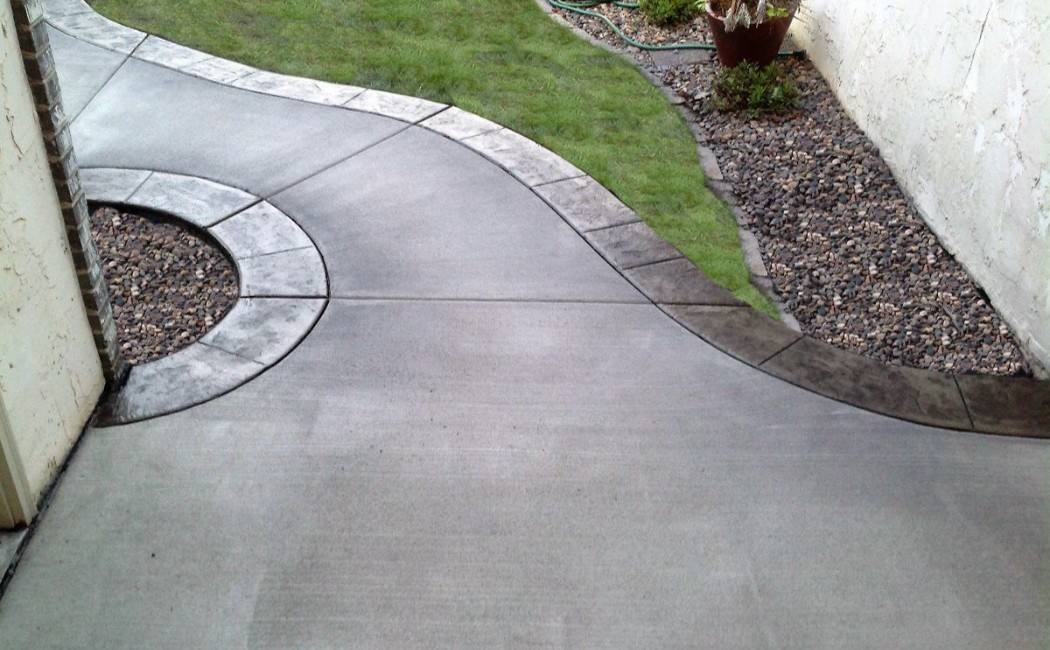 Curved, decorative concrete walkway bordered by landscaping stones, highlighting expert residential Concrete Sidewalk Services.
