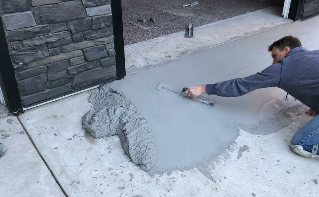 A worker is smoothing freshly poured concrete as part of a driveway repair. Concrete driveway repair services ensure a seamless, durable surface.