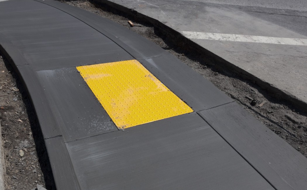 Newly installed concrete sidewalk ramp with a bright yellow tactile pad, showcasing professional Concrete Sidewalk Services for accessibility.