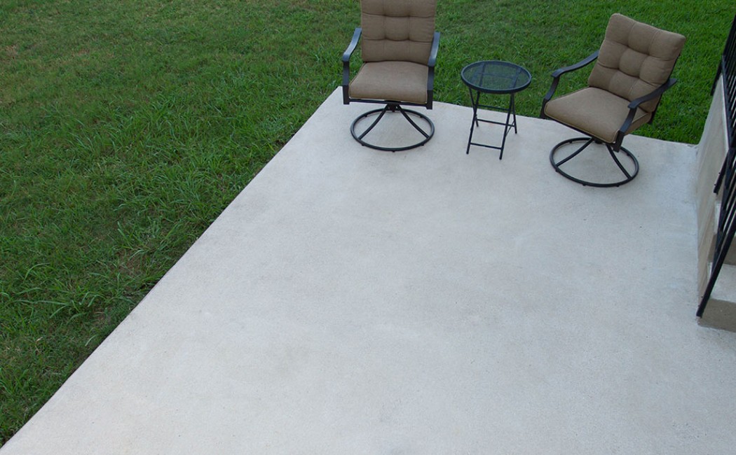 Minimalist outdoor seating setup on a smooth concrete patio beside a lawn, showcasing reliable Concrete Patios Services for clean and functional outdoor spaces.