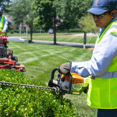 Professionals performing landscape repair services by trimming hedges and mowing lawns to restore a healthy, well-maintained outdoor space