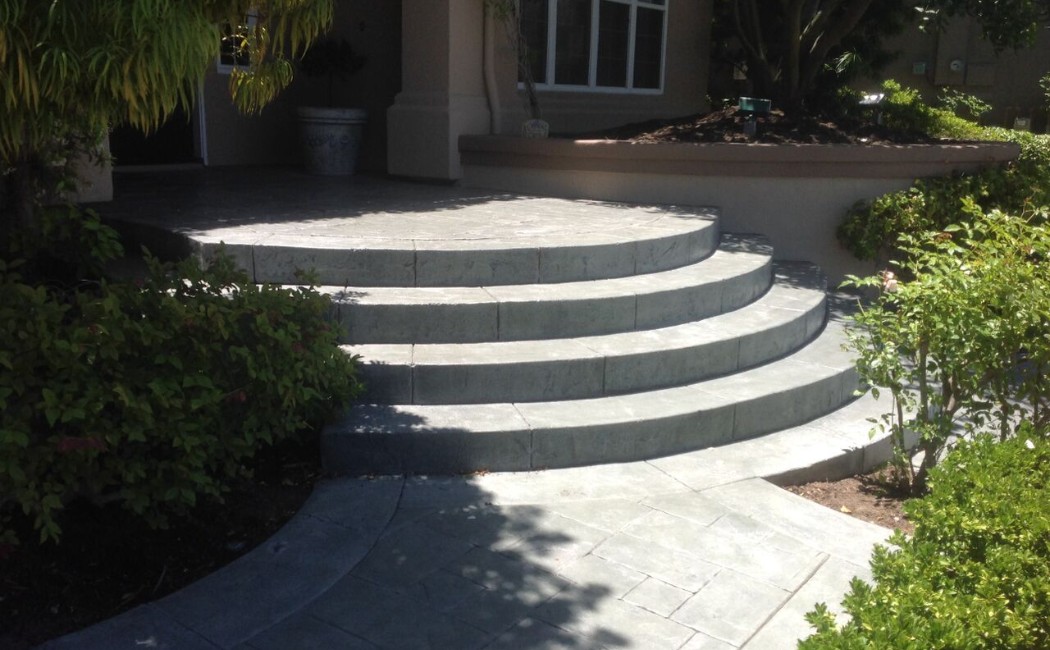 Curved concrete patio steps and walkway leading to a home entrance, showcasing professional Concrete Patios Services with a clean, modern finish.
