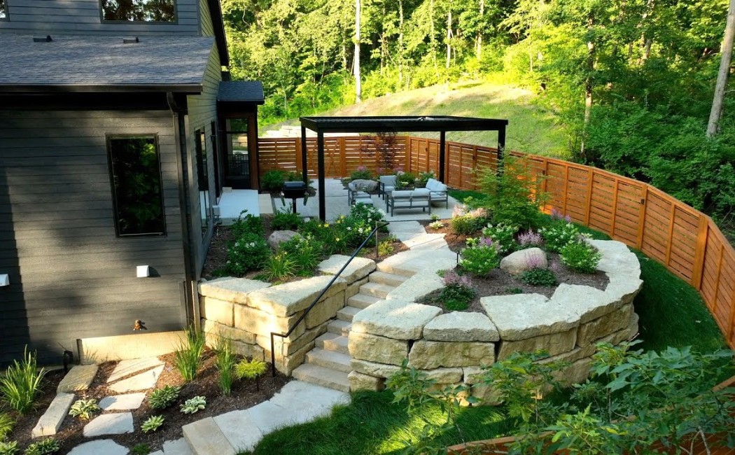 Modern backyard featuring a stone terrace, pergola seating area, retaining walls, and lush greenery designed with professional Landscape Installation Services.