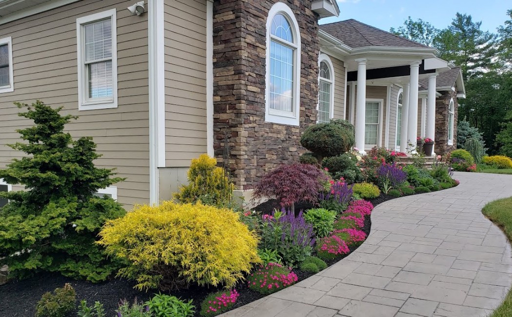 Elegant front yard with colorful flower beds, trimmed shrubs, and a paved walkway showcasing expert Landscape Installation Services for enhanced curb appeal.