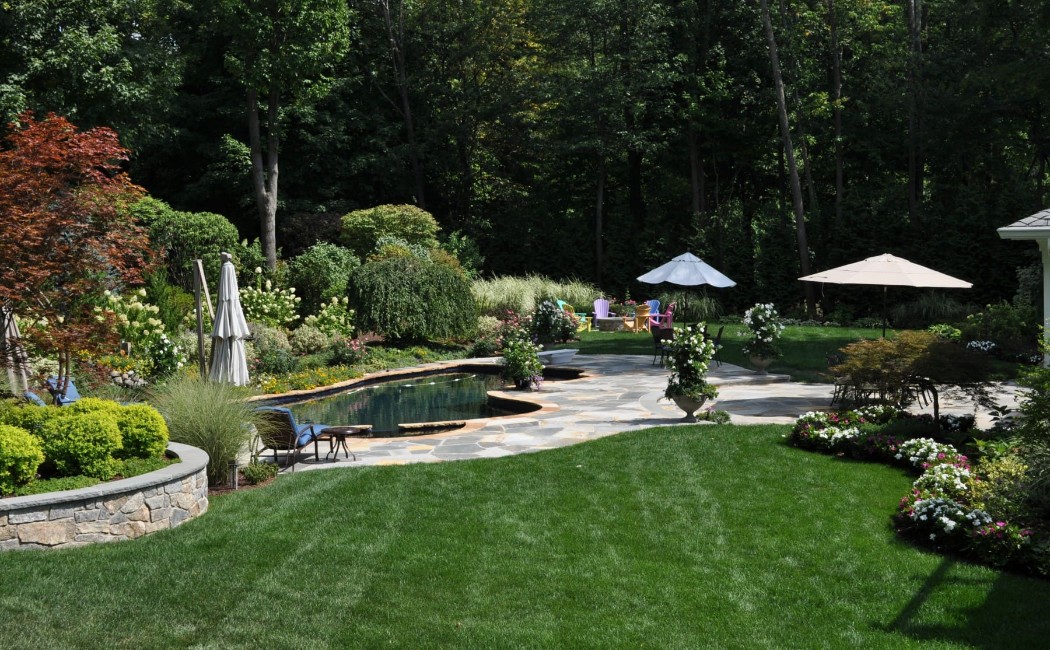 A beautifully restored backyard showcasing landscape repair services with lush green lawns, stone pathways, vibrant plants, and a well-maintained outdoor living area.